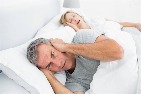 snoring couple - Annoyed man blocking his ears from noise of wife snoring at home in bedroom Photographie de stock - Aubaine LD & Abonnement, Code: 400-06931242