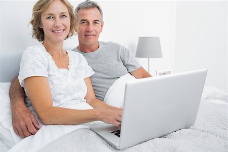 Relaxed couple using their laptop together in bed smiling at camera at home in bedroom Stock Photo - Budget Royalty-Free & Subscription, Code: 400-06931275