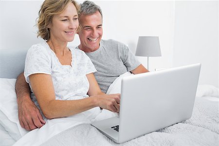 Smiling couple using their laptop together in bed at home in bedroom Stock Photo - Budget Royalty-Free & Subscription, Code: 400-06931272