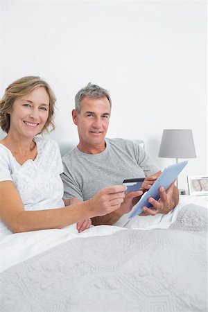 Smiling couple using their tablet pc to buy online looking at camera at home in bedroom Stock Photo - Budget Royalty-Free & Subscription, Code: 400-06931284