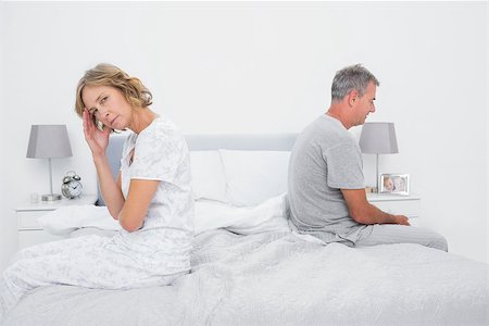 Annoyed couple sitting on different sides of bed having a dispute with woman looking at camera in bedroom at home Stock Photo - Budget Royalty-Free & Subscription, Code: 400-06931304