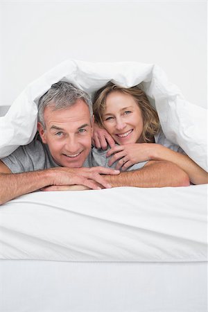 simsearch:400-06891126,k - Cheerful middle aged couple under the duvet smiling at camera in bedroom at home Stock Photo - Budget Royalty-Free & Subscription, Code: 400-06931317