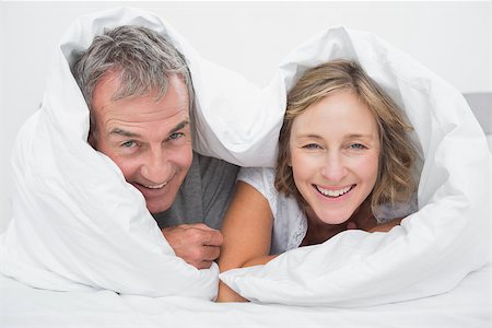 simsearch:400-06891126,k - Happy middle aged couple under the duvet smiling at camera in bedroom at home Stock Photo - Budget Royalty-Free & Subscription, Code: 400-06931318