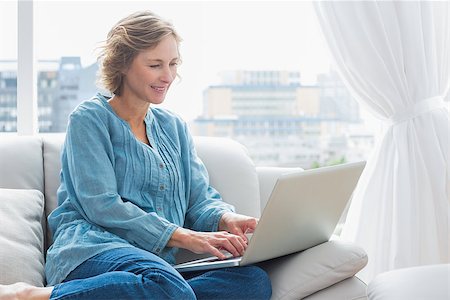 simsearch:400-06872352,k - Happy blonde woman sitting on her couch using laptop at home in the sitting room Foto de stock - Royalty-Free Super Valor e Assinatura, Número: 400-06931335