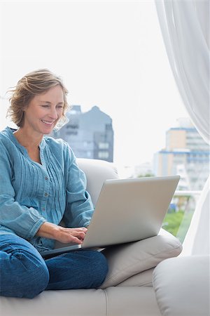 simsearch:400-06872352,k - Smiling blonde woman sitting on her couch using laptop at home in the sitting room Foto de stock - Royalty-Free Super Valor e Assinatura, Número: 400-06931336