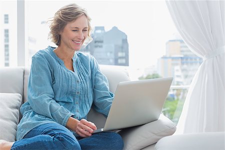 simsearch:400-06872352,k - Cheerful blonde woman sitting on her couch using laptop at home in the sitting room Foto de stock - Royalty-Free Super Valor e Assinatura, Número: 400-06931337