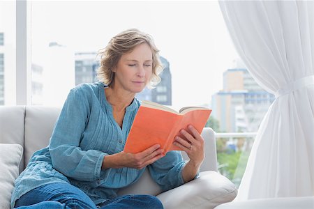 simsearch:400-06872352,k - Cheerful blonde woman sitting on her couch reading a book at home in the sitting room Foto de stock - Royalty-Free Super Valor e Assinatura, Número: 400-06931338