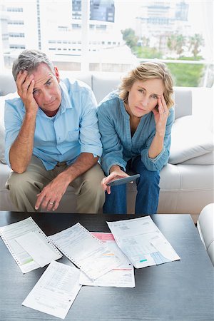 simsearch:400-07333928,k - Anxious couple sitting on their couch paying their bills looking at camera at home in the living room Stock Photo - Budget Royalty-Free & Subscription, Code: 400-06931529