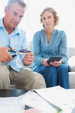 simsearch:400-07333928,k - Husband cutting credit card in half with wife with bills on the table at home in the living room Stock Photo - Budget Royalty-Free & Subscription, Code: 400-06931534