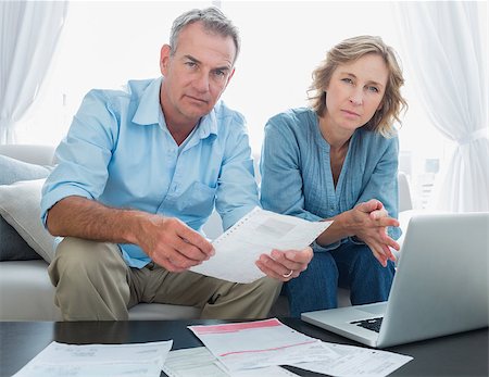 simsearch:400-07333928,k - Worried couple paying their bills online with laptop looking at camera at home in the living room Stock Photo - Budget Royalty-Free & Subscription, Code: 400-06931539