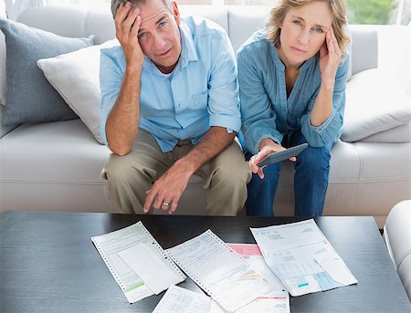 simsearch:400-07333928,k - Stressed couple sitting on their couch paying their bills smiling at camera at home in the living room Stock Photo - Budget Royalty-Free & Subscription, Code: 400-06931530