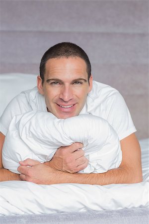 simsearch:6109-08489191,k - Cheerful man hugging his pillow smiling at camera at home in the bedroom Fotografie stock - Microstock e Abbonamento, Codice: 400-06931591