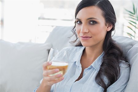 Pretty brunette drinking white wine sitting on sofa in her living room Stock Photo - Budget Royalty-Free & Subscription, Code: 400-06933465