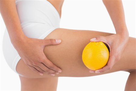 skin and fit - Slim woman squeezing cellulite skin on thigh as she holds orange on white background Stock Photo - Budget Royalty-Free & Subscription, Code: 400-06933675