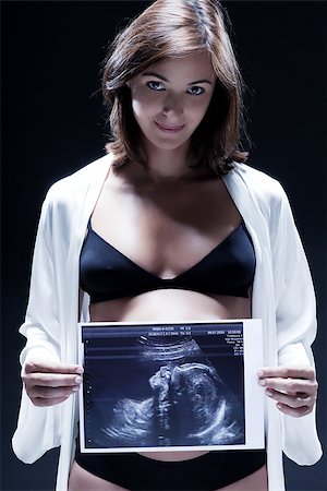pregnant scan - smiling caucasian pregnant holding ultrasound scan  woman portraitt  in nightie on studio isolated black background Foto de stock - Super Valor sin royalties y Suscripción, Código: 400-06948928