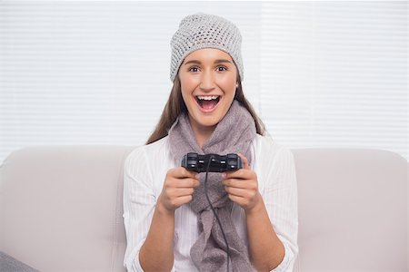 Smiling brunette with winter hat on playing video games sitting on cosy sofa Stock Photo - Budget Royalty-Free & Subscription, Code: 400-06956145