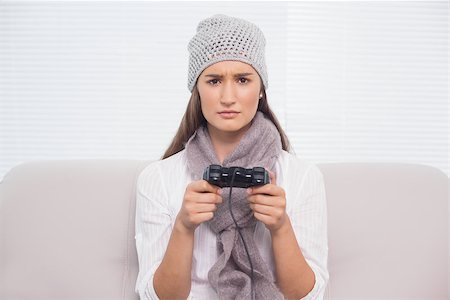 Frowning brunette with winter hat on playing video games sitting on cosy sofa Stock Photo - Budget Royalty-Free & Subscription, Code: 400-06956146