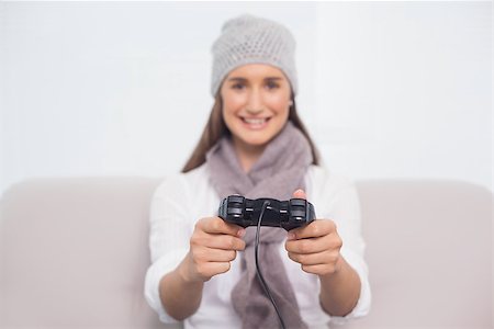 Cheerful brunette with winter hat on playing video games sitting on cosy sofa Stock Photo - Budget Royalty-Free & Subscription, Code: 400-06956147