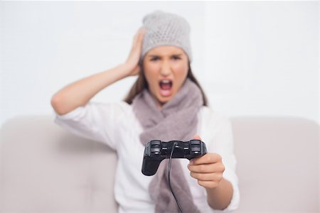 Furious brunette with winter hat on playing video games sitting on cosy sofa Stock Photo - Budget Royalty-Free & Subscription, Code: 400-06956148