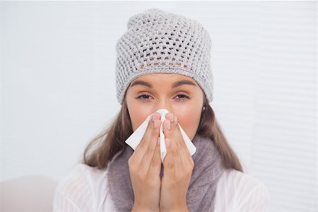 simsearch:400-06801081,k - Sick brunette with winter hat on blowing her nose sitting on cosy sofa Photographie de stock - Aubaine LD & Abonnement, Code: 400-06956141