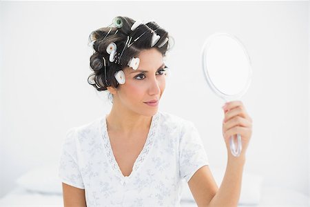 Happy brunette in hair rollers holding hand mirror at home in bedroom Photographie de stock - Aubaine LD & Abonnement, Code: 400-06958198