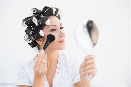 Pretty brunette in hair rollers holding hand mirror and applying makeup at home in bedroom Stock Photo - Budget Royalty-Free & Subscription, Code: 400-06958205