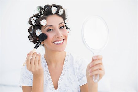 Smiling brunette in hair rollers holding hand mirror and applying makeup at home in bedroom Stock Photo - Budget Royalty-Free & Subscription, Code: 400-06958206