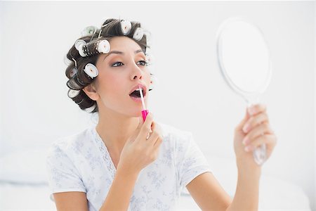Pretty brunette in hair rollers holding hand mirror and applying lip gloss at home in bedroom Stock Photo - Budget Royalty-Free & Subscription, Code: 400-06958209