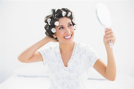 Happy brunette in hair rollers looking in hand mirror at home in bedroom Stock Photo - Budget Royalty-Free & Subscription, Code: 400-06958200