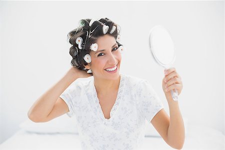 Smiling brunette in hair rollers holding hand mirror at home in bedroom Stock Photo - Budget Royalty-Free & Subscription, Code: 400-06958201
