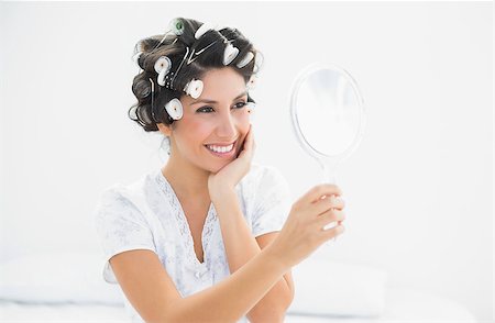 Smiling brunette in hair rollers looking in hand mirror at home in bedroom Stock Photo - Budget Royalty-Free & Subscription, Code: 400-06958202