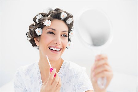 Happy brunette in hair rollers looking in hand mirror and holding  lip gloss at home in bedroom Photographie de stock - Aubaine LD & Abonnement, Code: 400-06958211