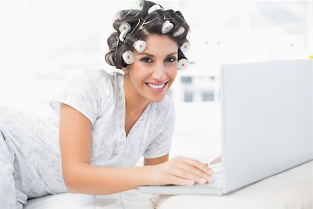 simsearch:693-06323945,k - Cheerful brunette in hair rollers lying on her bed using her laptop in bedroom at home Stock Photo - Budget Royalty-Free & Subscription, Code: 400-06958233