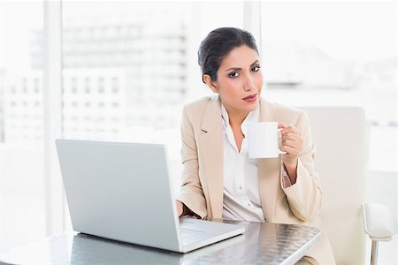 Smiling businesswoman holding mug while working on laptop at the office Photographie de stock - Aubaine LD & Abonnement, Code: 400-06958809