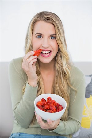 Happy cute blonde eating strawberries sitting on cosy sofa in bright living room Stock Photo - Budget Royalty-Free & Subscription, Code: 400-06959751