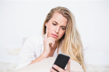 simsearch:693-07542343,k - Frowning model holding her smartphone lying on cosy bed in bright bedroom Stock Photo - Budget Royalty-Free & Subscription, Code: 400-06960014