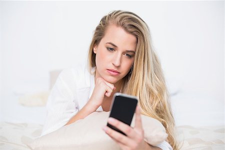simsearch:693-07542343,k - Pensive gorgeous model looking at her smartphone lying on cosy bed in bright bedroom Stock Photo - Budget Royalty-Free & Subscription, Code: 400-06960010