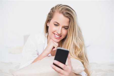 simsearch:693-07542343,k - Smiling gorgeous model looking at her smartphone lying on cosy bed in bright bedroom Stock Photo - Budget Royalty-Free & Subscription, Code: 400-06960011