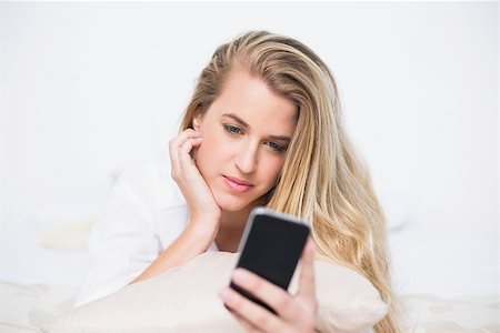 simsearch:693-07542343,k - Content gorgeous model looking at her smartphone lying on cosy bed in bright bedroom Stock Photo - Budget Royalty-Free & Subscription, Code: 400-06960012