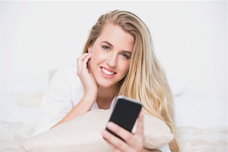 simsearch:693-07542343,k - Smiling model holding her smartphone lying on cosy bed in bright bedroom Stock Photo - Budget Royalty-Free & Subscription, Code: 400-06960013