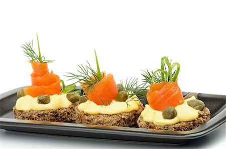 simsearch:400-07039898,k - Arrangement of Snacks with Smoked Salmon, Greens, Cheese Cream and Capers on Black Plate isolated on white background Foto de stock - Royalty-Free Super Valor e Assinatura, Número: 400-07039900