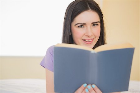 simsearch:400-06932687,k - Cheerful brunette looking at camera and lying on a bed reading a book in a bedroom Stock Photo - Budget Royalty-Free & Subscription, Code: 400-07057521