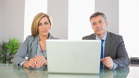 simsearch:400-04186486,k - Two severe mature business people looking at camera behind an opened laptop at office Stock Photo - Budget Royalty-Free & Subscription, Code: 400-07057729