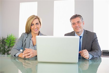 simsearch:400-04186486,k - Two smiling mature business people looking at camera behind an opened laptop at office Stock Photo - Budget Royalty-Free & Subscription, Code: 400-07057730
