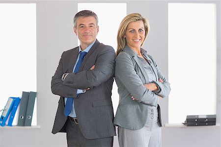 simsearch:400-07275828,k - Two smiling mature businesspeople looking at camera standing firmly back to back with crossed arms at office Photographie de stock - Aubaine LD & Abonnement, Code: 400-07057752