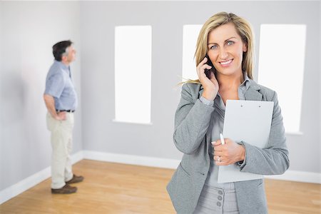 simsearch:400-07475963,k - Happy realtor calling someone with her mobile phone in empty house with potential buyer smiling at camera Stock Photo - Budget Royalty-Free & Subscription, Code: 400-07057782