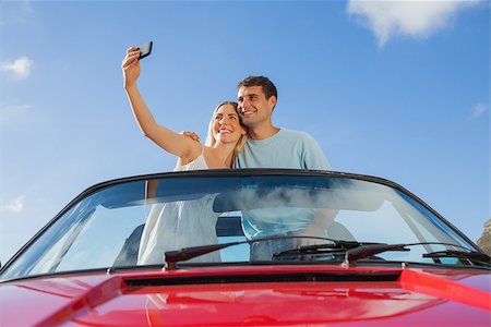 simsearch:400-07058116,k - Cheerful couple standing in red cabriolet taking picture on a sunny day Stock Photo - Budget Royalty-Free & Subscription, Code: 400-07058174