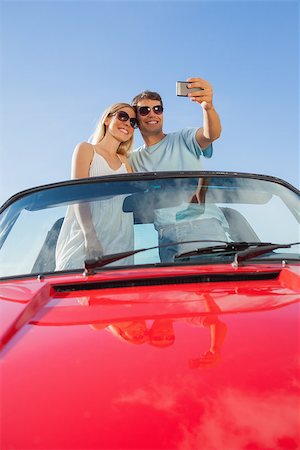 simsearch:400-07058116,k - Smiling couple standing in red cabriolet taking picture on a sunny day Stock Photo - Budget Royalty-Free & Subscription, Code: 400-07058173