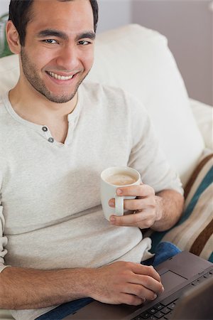 simsearch:6109-08581996,k - Smiling attractive man drinking coffee while using his laptop in bright living room Fotografie stock - Microstock e Abbonamento, Codice: 400-07058747