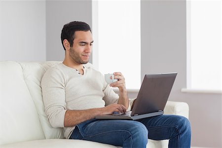 simsearch:6109-08581996,k - Relaxed attractive man holding coffee while working on his laptop in bright living room Fotografie stock - Microstock e Abbonamento, Codice: 400-07058742